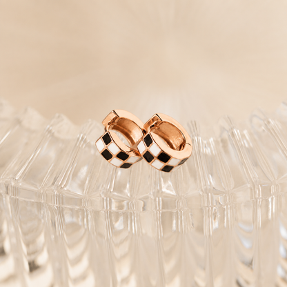 Rose gold hoop earrings with black checkered pattern on a beige background