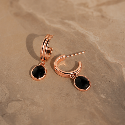 Rose gold hoop earrings with black stones on a beige stone surface