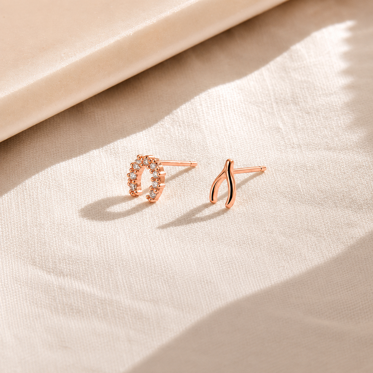 Two rose gold earrings on a beige fabric background