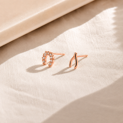 Two rose gold earrings on a beige fabric background