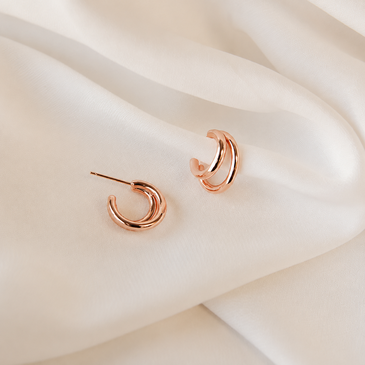 Rose gold hoop earrings on a soft beige fabric background