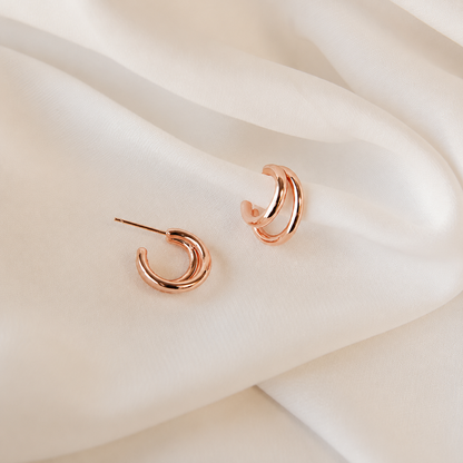Rose gold hoop earrings on a soft beige fabric background