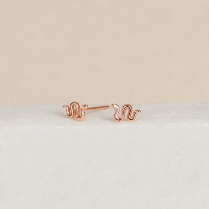 Rose gold snake-shaped earrings on a light beige background