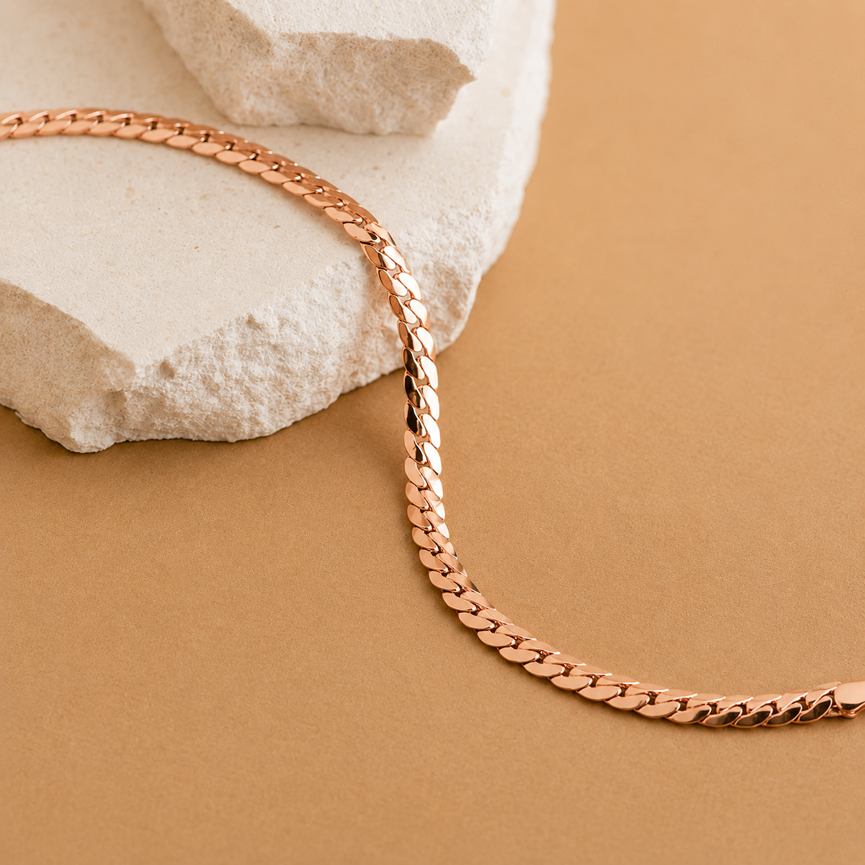 Rose gold chain necklace on a beige surface with a stone background
