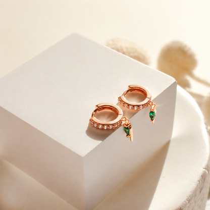Rose gold earrings with green gemstones on a white surface