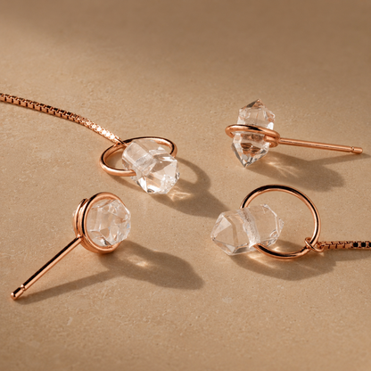 Jewelry set with rose gold necklaces and clear crystal pendants on a beige background