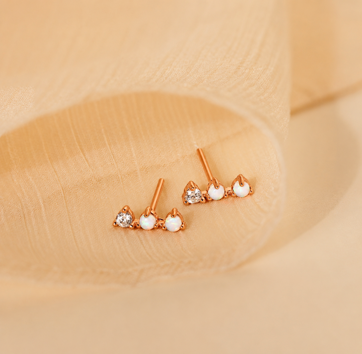 Rose gold earrings with heart and gemstone designs on a beige background
