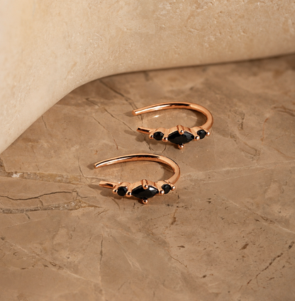 Rose gold ear cuffs with black gemstones on a beige stone surface