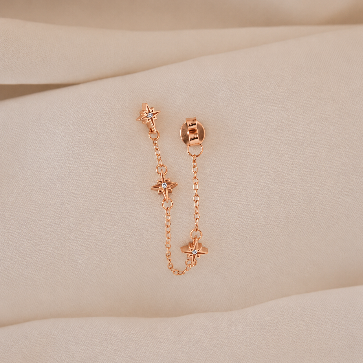 Rose gold chain earrings on a beige surface
