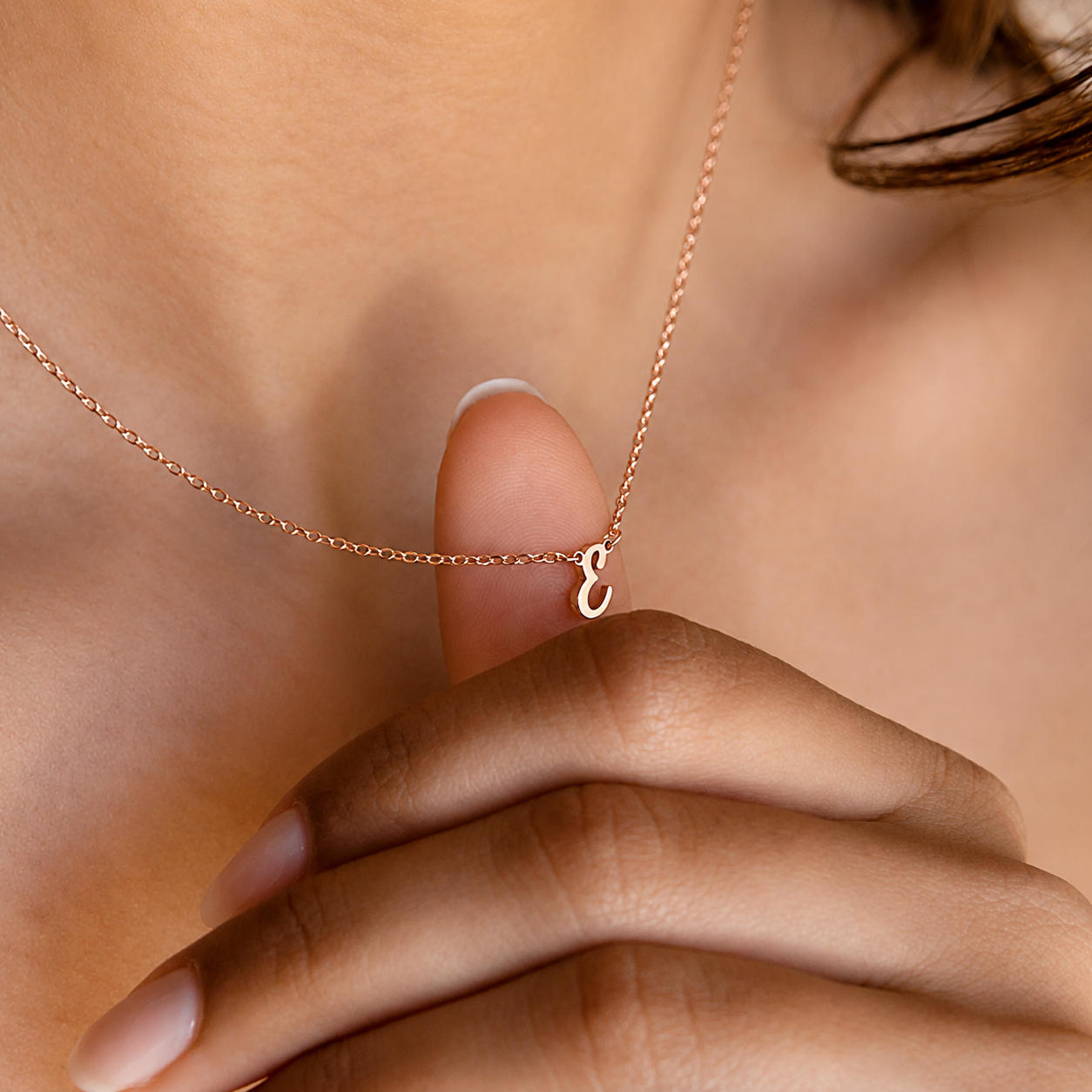 Rose gold necklace with a small 'c' pendant held by a hand against a neutral background