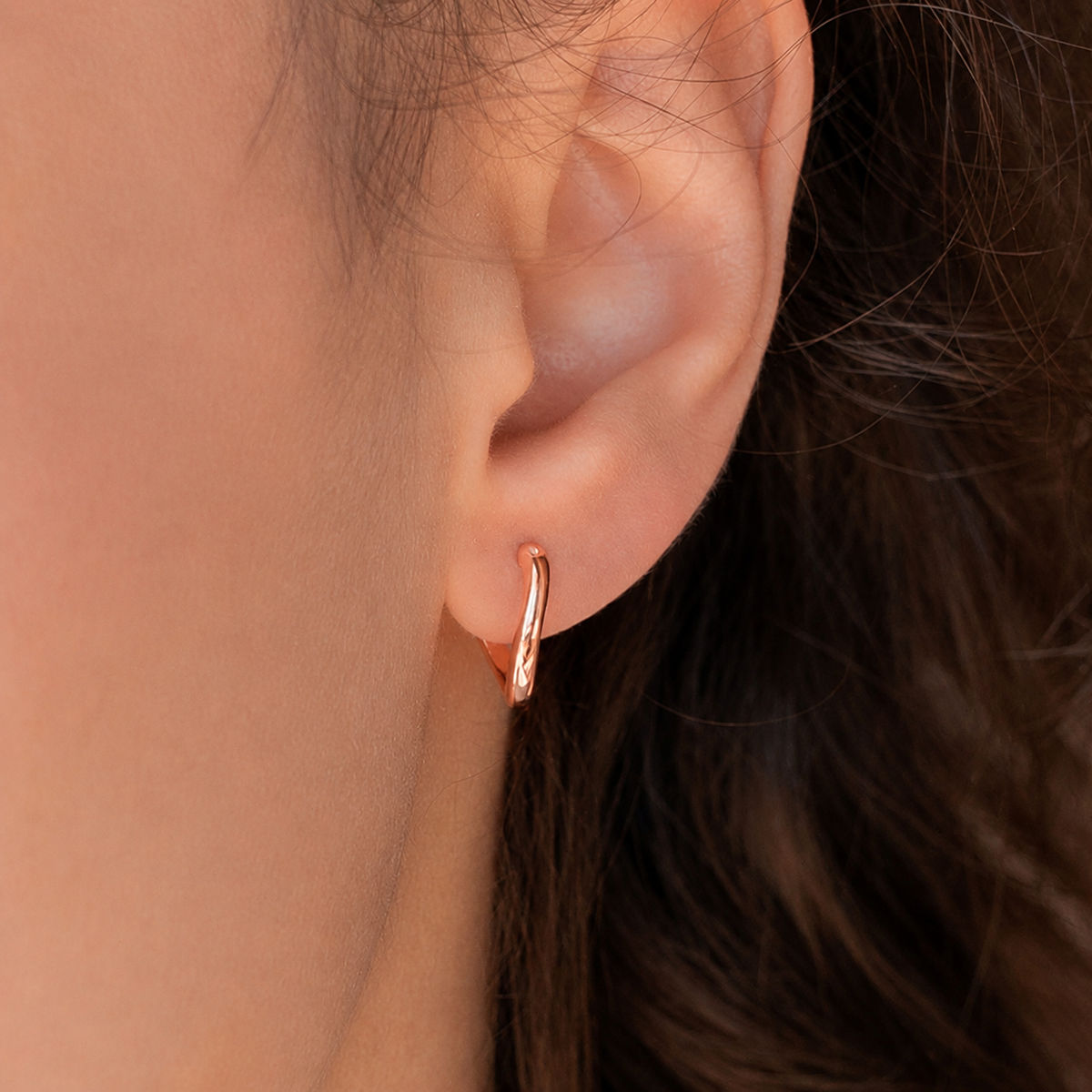 Close-up of an ear wearing a rose gold hoop earring with blurred background
