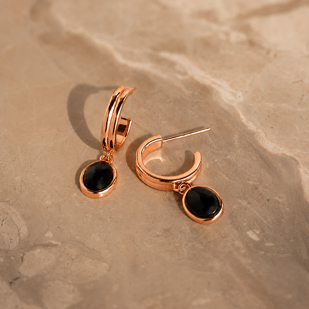 Rose gold hoop earrings with black stones on a beige stone surface