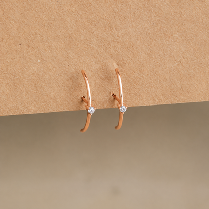 Rose gold hoop earrings with small diamonds on a beige background