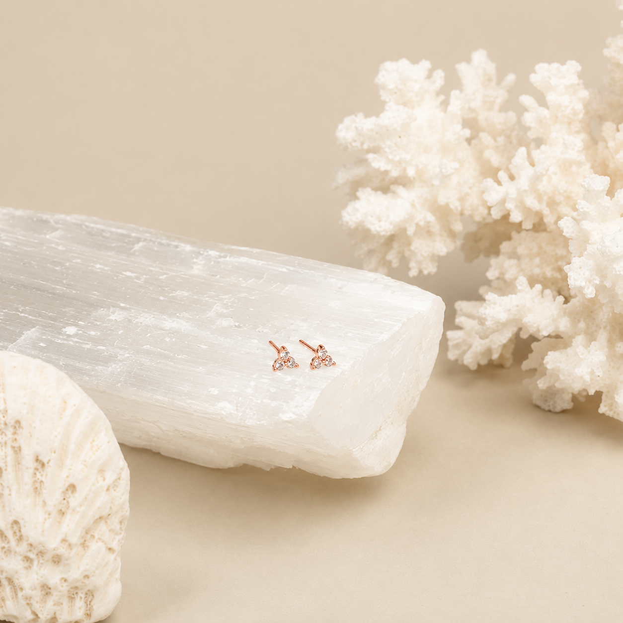 Rose gold earrings on a piece of crystal with coral and shells in the background