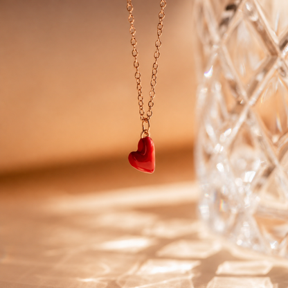 Gold necklace with a red heart pendant against a warm-toned background