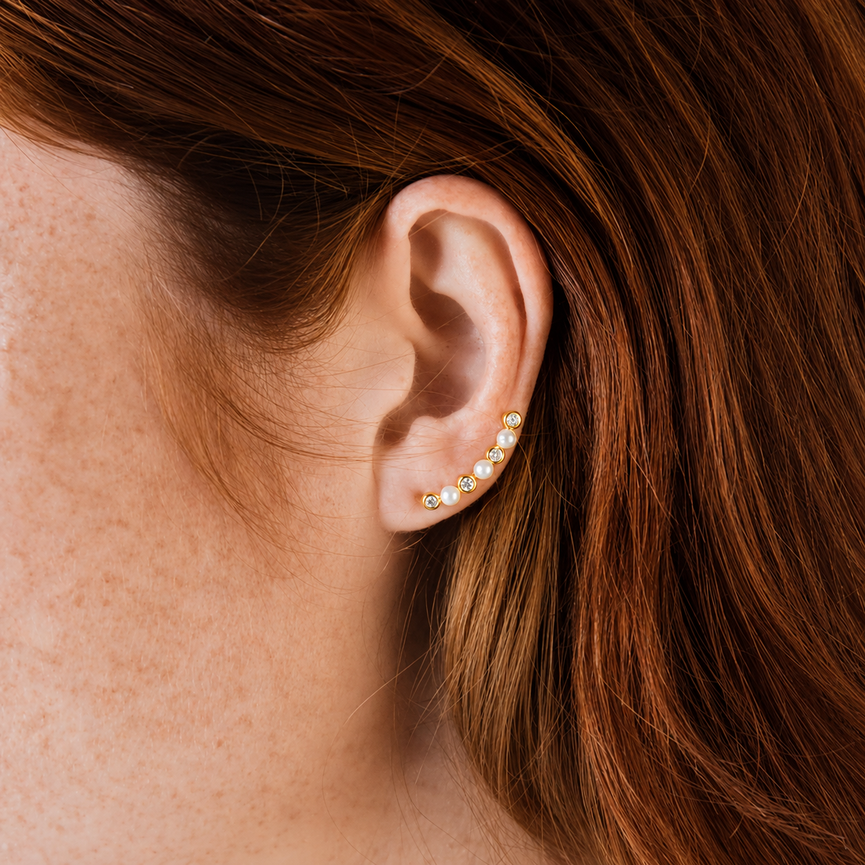 Close-up of an ear wearing a pearl earring with brown hair.