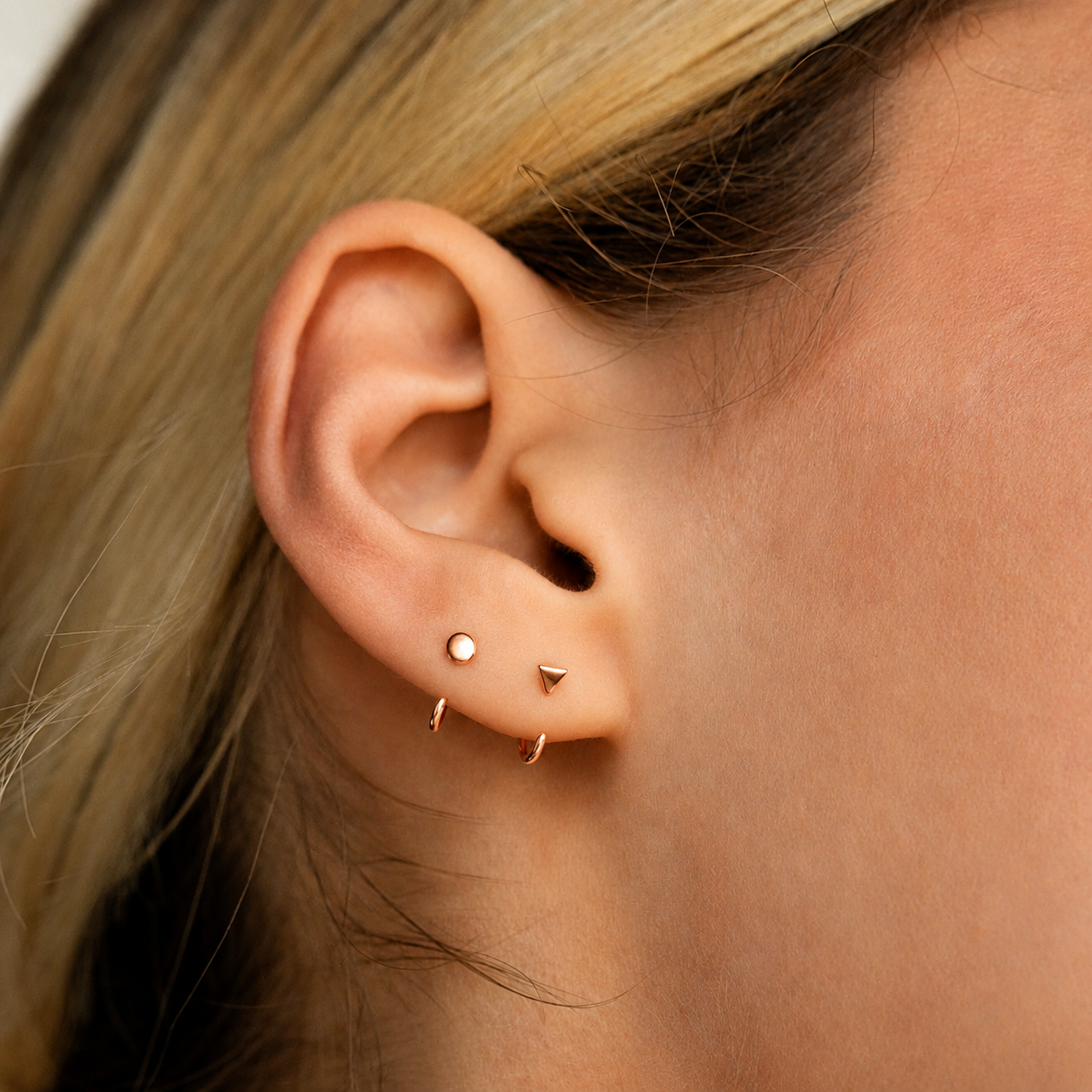 Close-up of an ear with gold earrings on a neutral background
