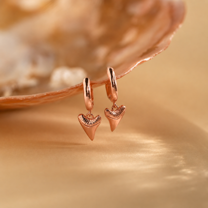 Rose gold shark tooth earrings on a gold background