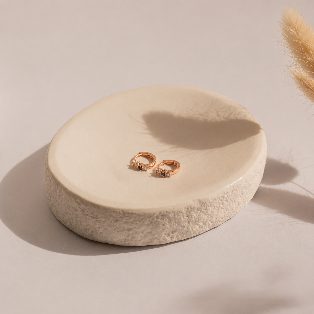 Pair of rose gold earrings on a round beige stone surface with a soft background