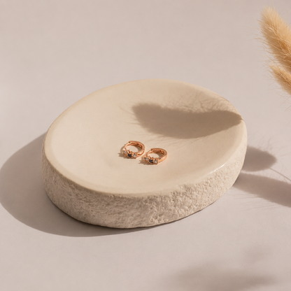 Pair of rose gold earrings on a round beige stone surface with a soft background