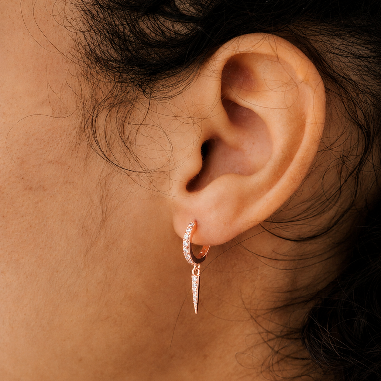 Close-up of an ear wearing a rose gold hoop earring with a dangling spike.