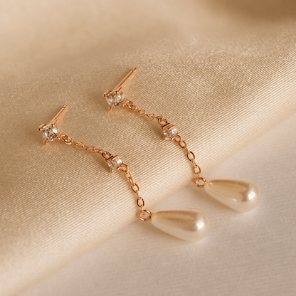 Rose gold earrings with pearl drops on a beige fabric background