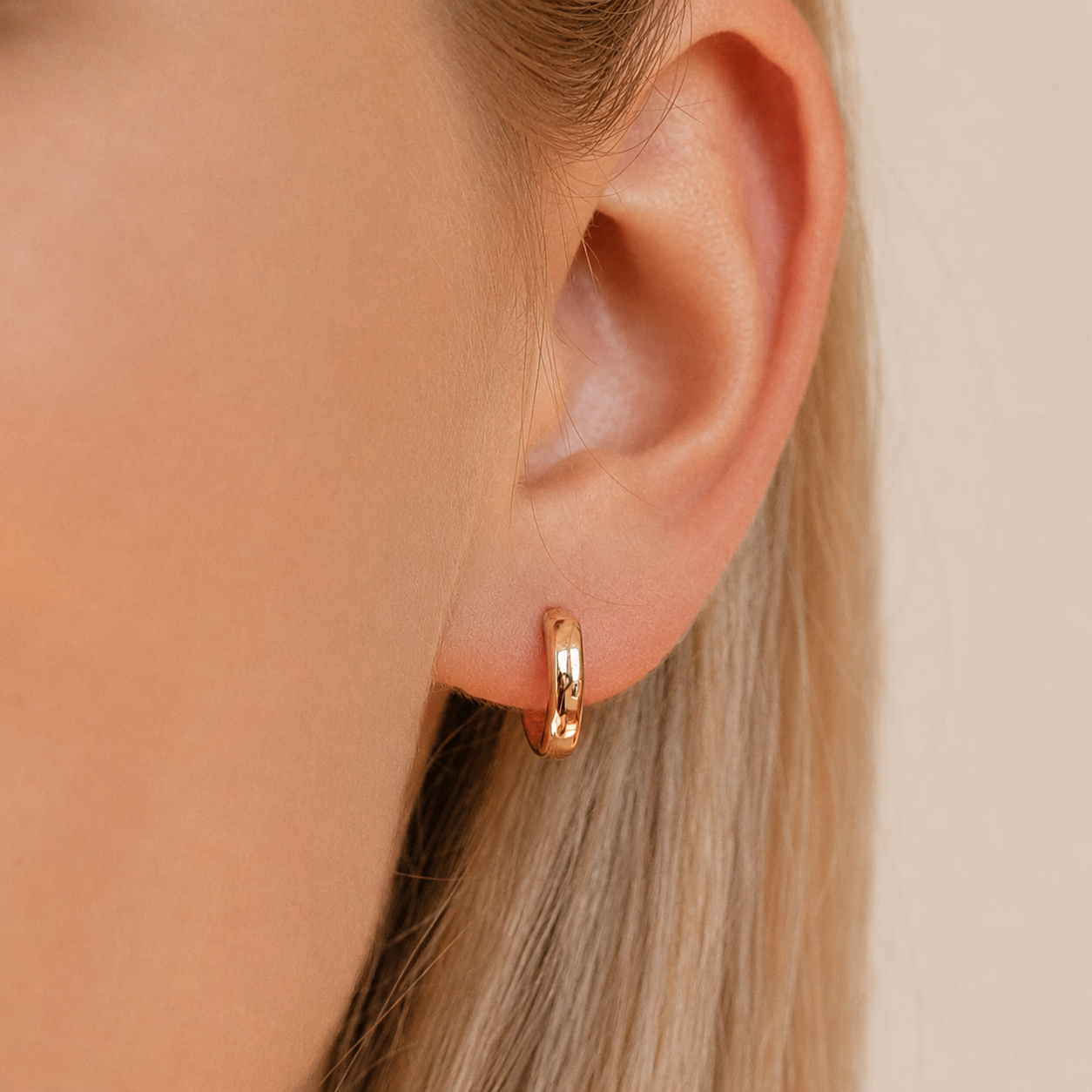 Gold hoop earring worn by a person with blonde hair against a neutral background