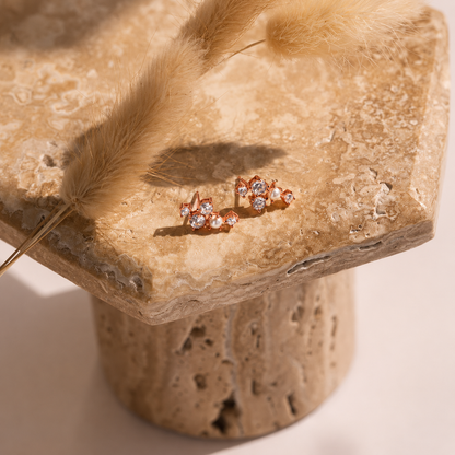 Pair of rose gold earrings with clear stones on a textured stone surface.