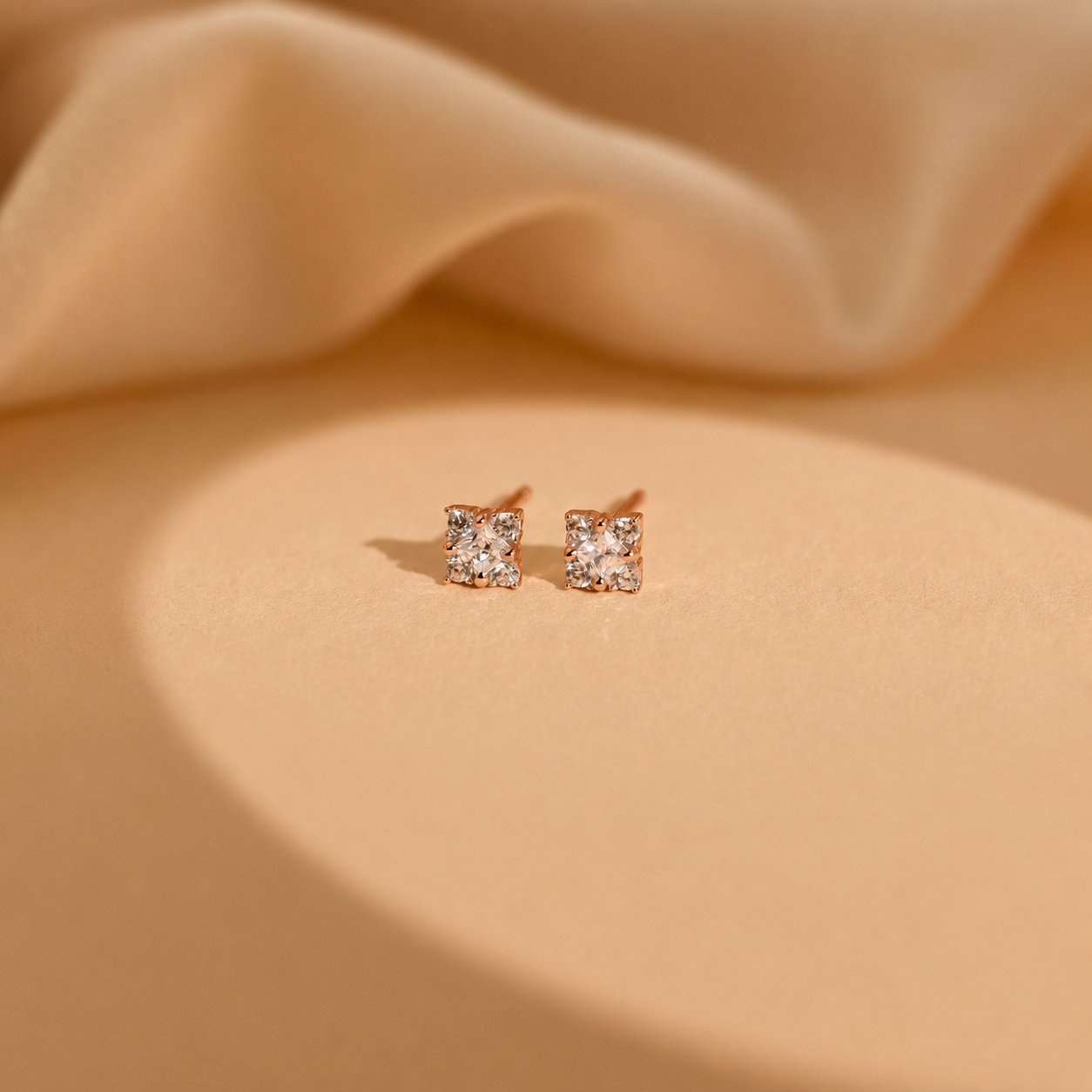 Pair of rose gold square stud earrings on beige fabric