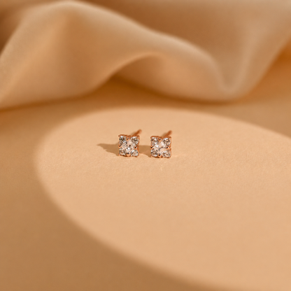 Pair of rose gold square stud earrings on beige fabric