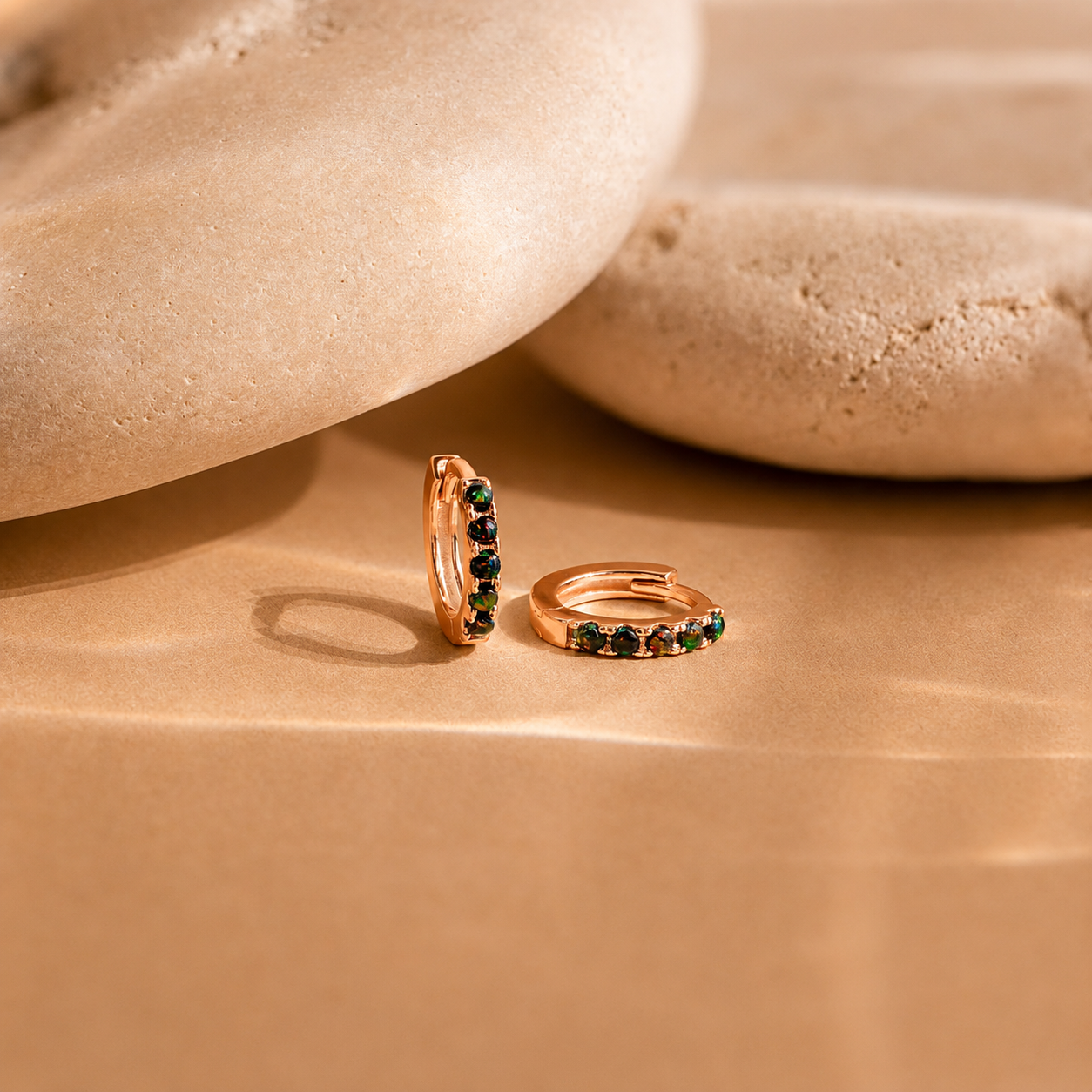 Rose gold hoop earrings with green gemstones on a beige stone surface