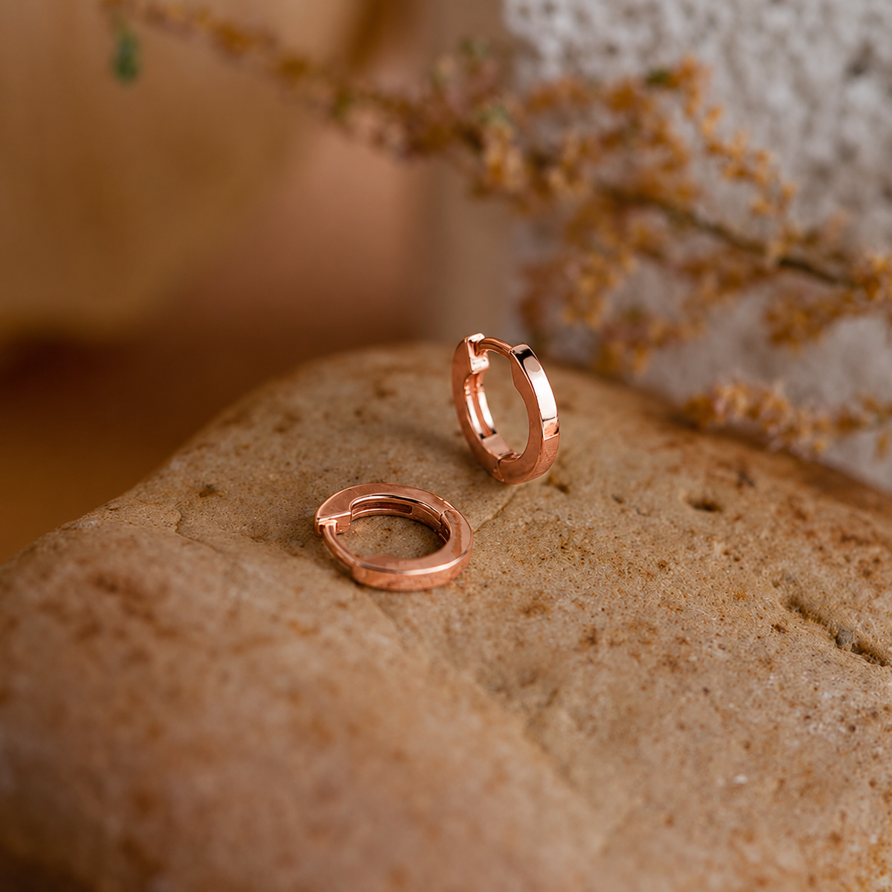 Rose gold hoop earrings on a textured surface with a blurred natural background