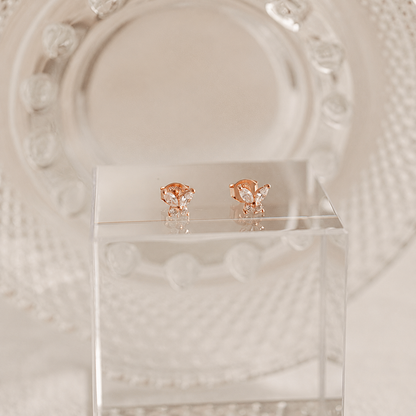 Rose gold butterfly earrings on a clear stand with a decorative white background