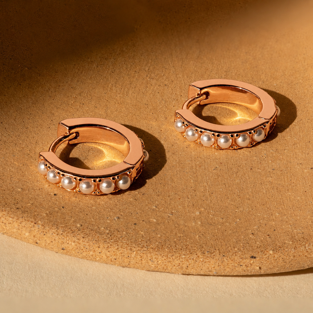 Rose gold hoop earrings with pearl accents on a beige surface