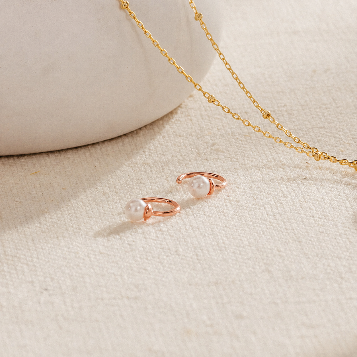 Rose gold earrings with a pearl-like center on a beige fabric background