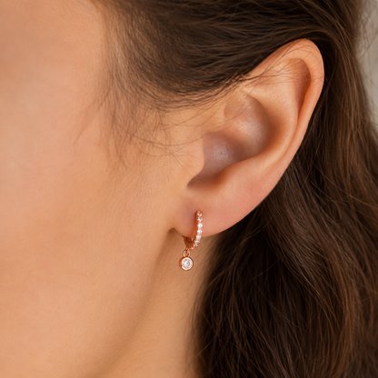Close-up of an ear wearing a rose gold earring with clear gemstones.