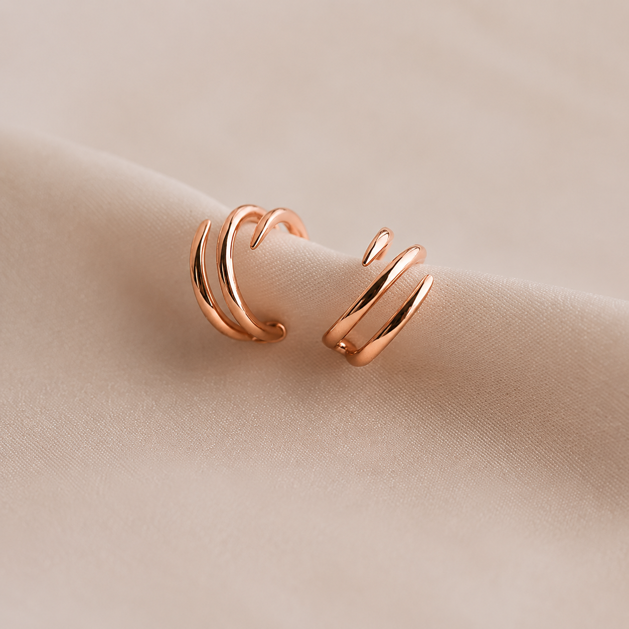 Rose gold hoop earrings on a beige fabric background
