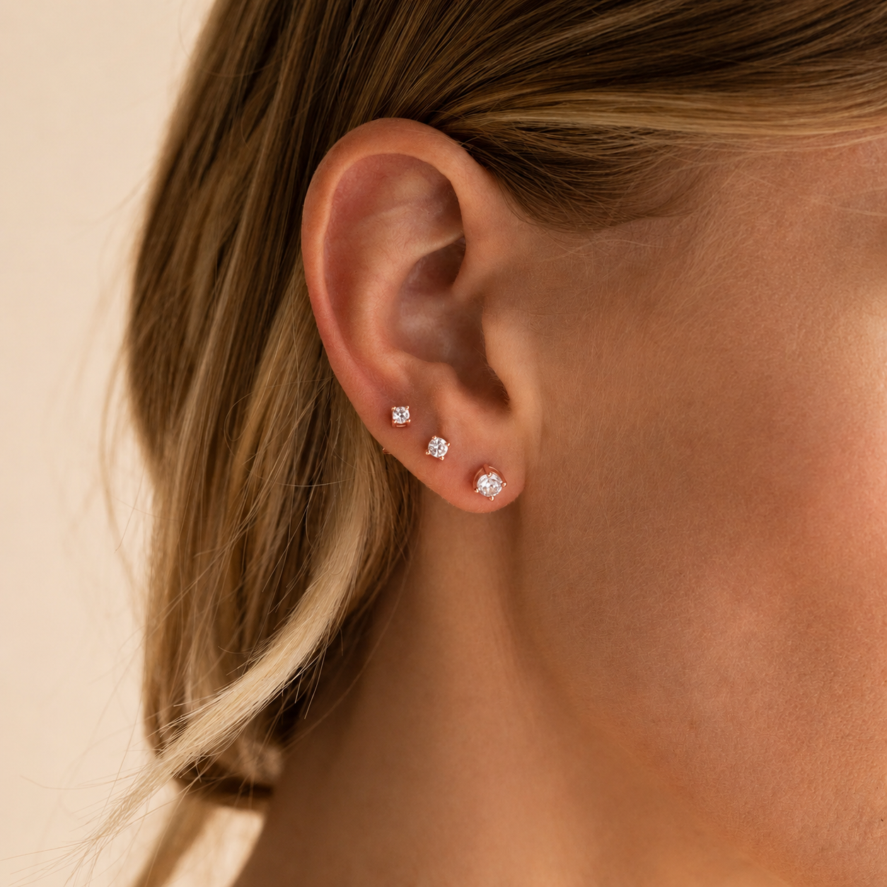 Close-up of an ear wearing diamond stud earrings on a neutral background