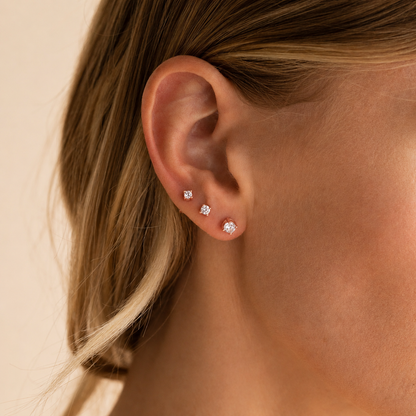 Close-up of an ear wearing diamond stud earrings on a neutral background