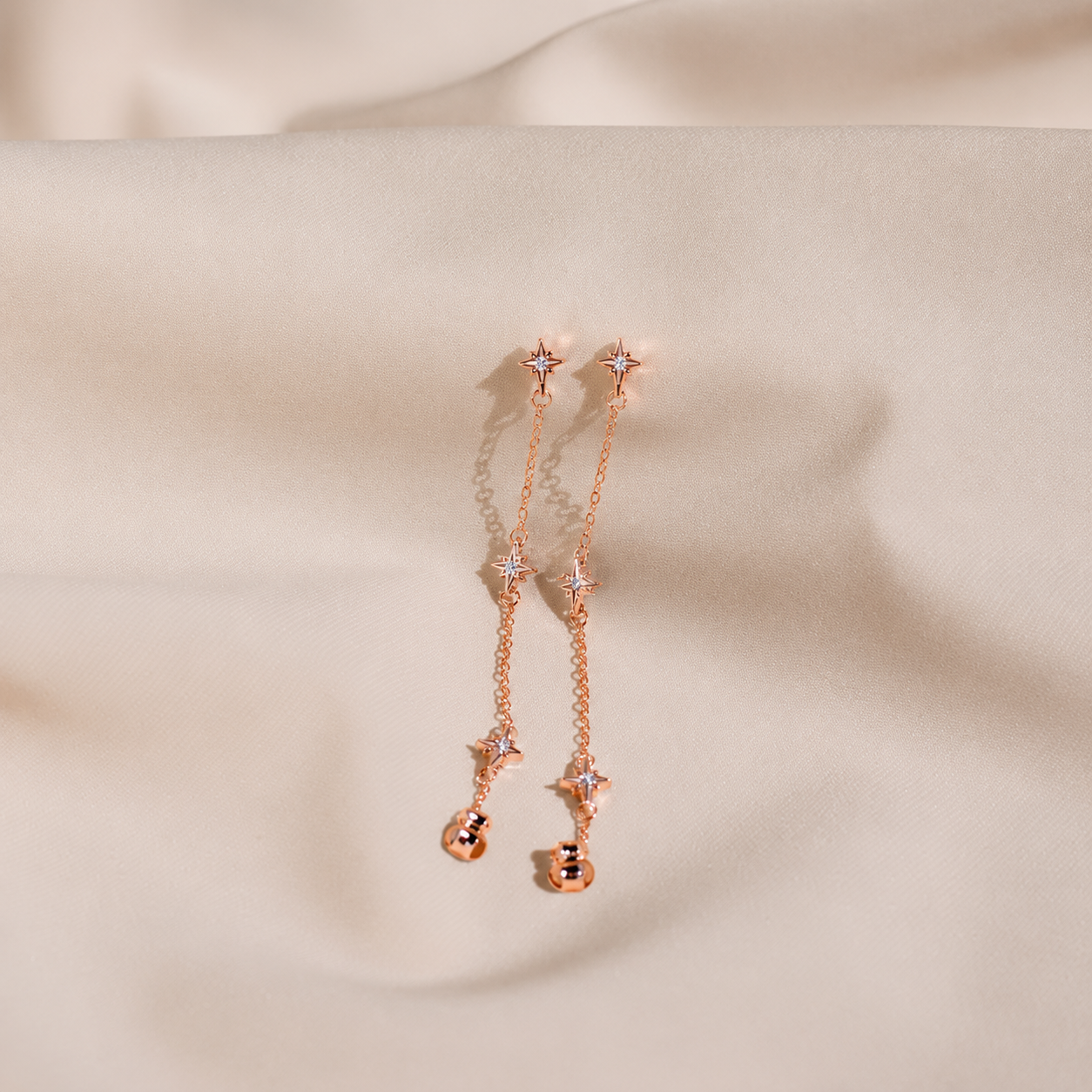 Rose gold earrings with star-shaped elements on a beige fabric background