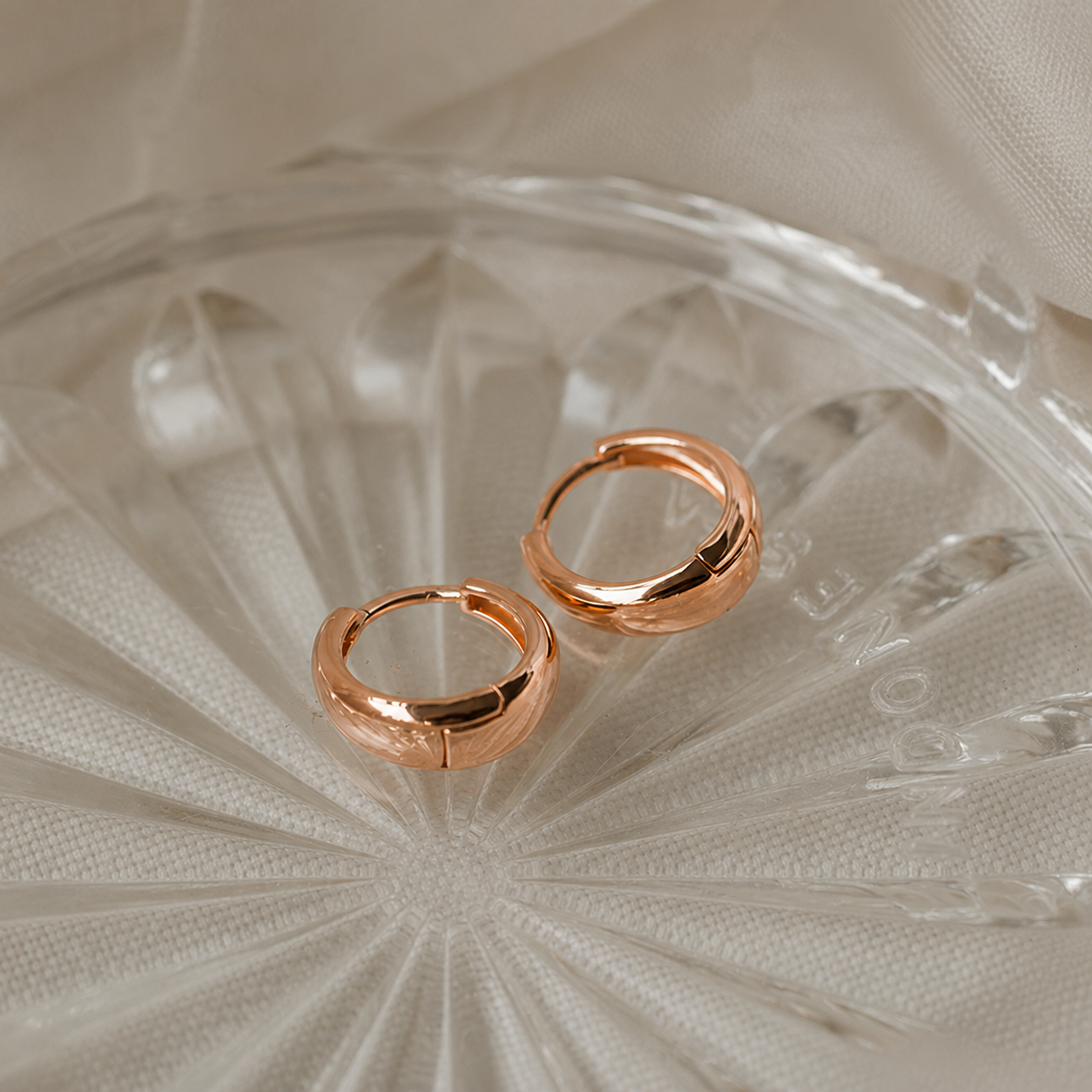 Rose gold hoop earrings on a textured glass surface