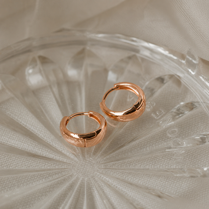Rose gold hoop earrings on a textured glass surface