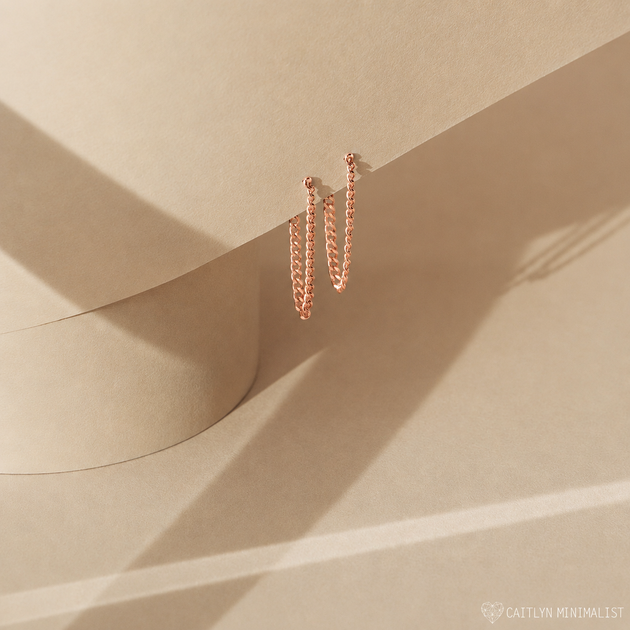 Rose gold hoop earrings on a beige surface with soft shadows