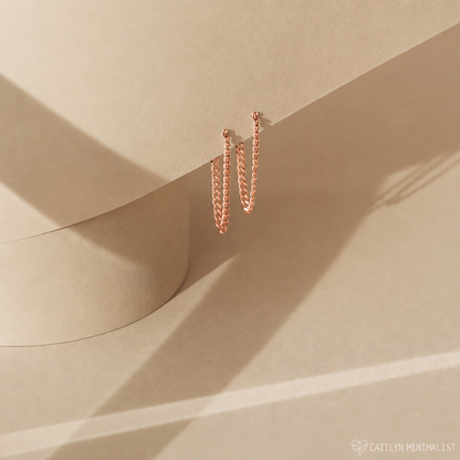 Rose gold hoop earrings on a beige surface with soft shadows