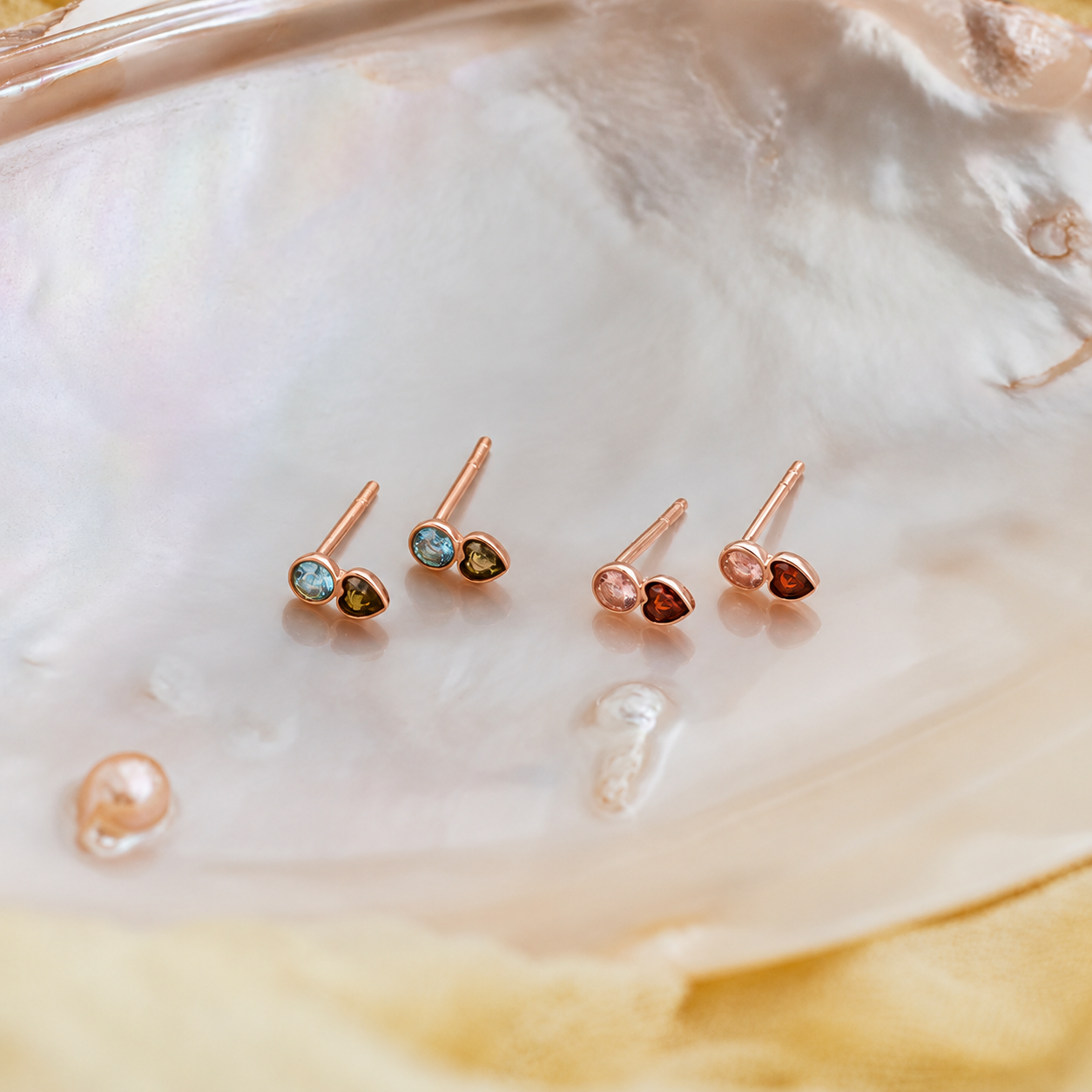 Set of small heart-shaped earrings with colored stones on a shell background