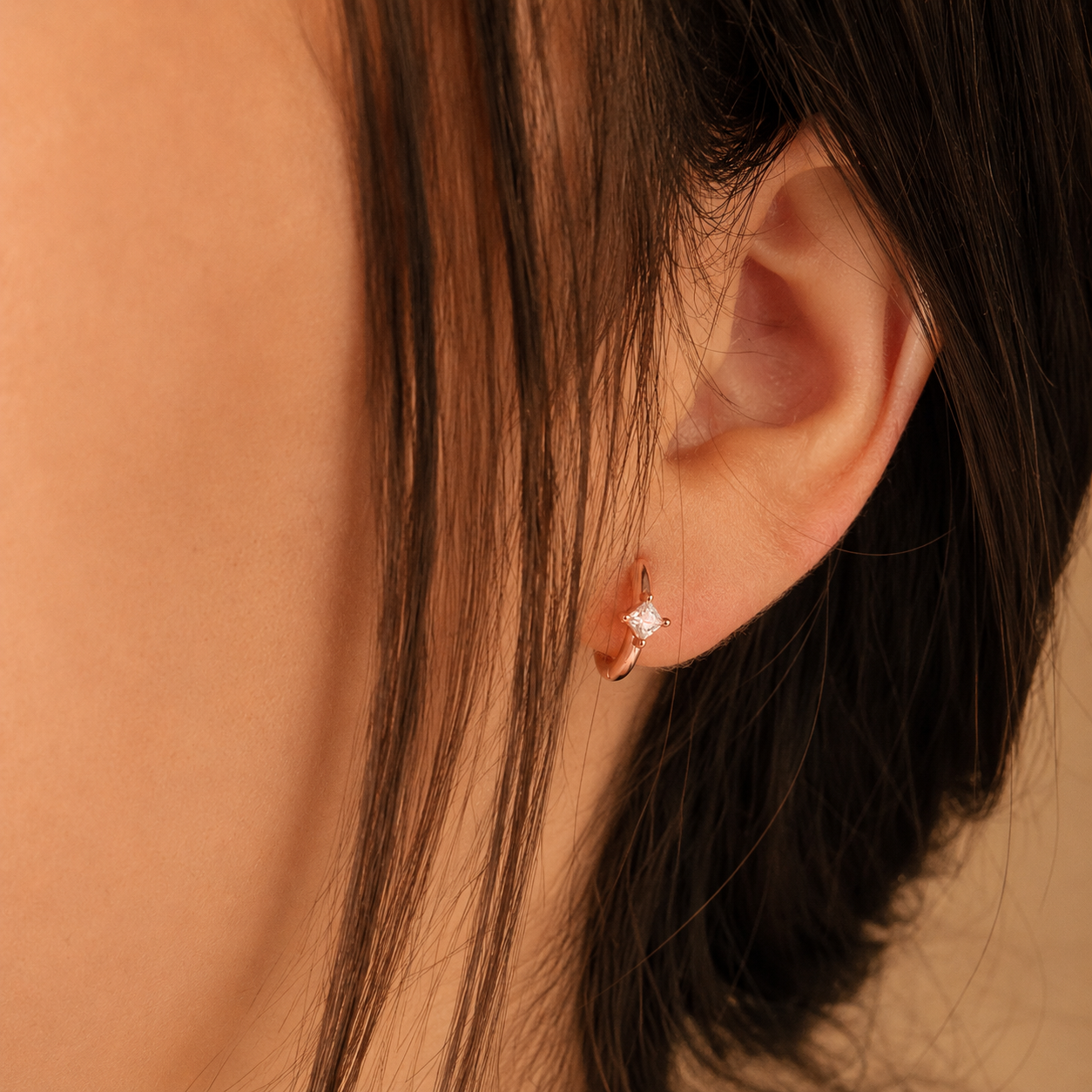 Close-up of an ear wearing a diamond earring with a blurred background