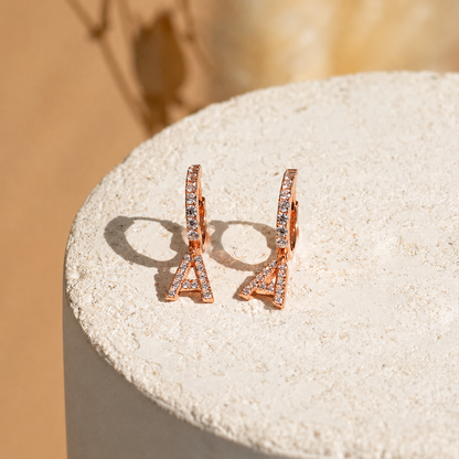 Rose gold earrings with small diamonds on a textured beige surface