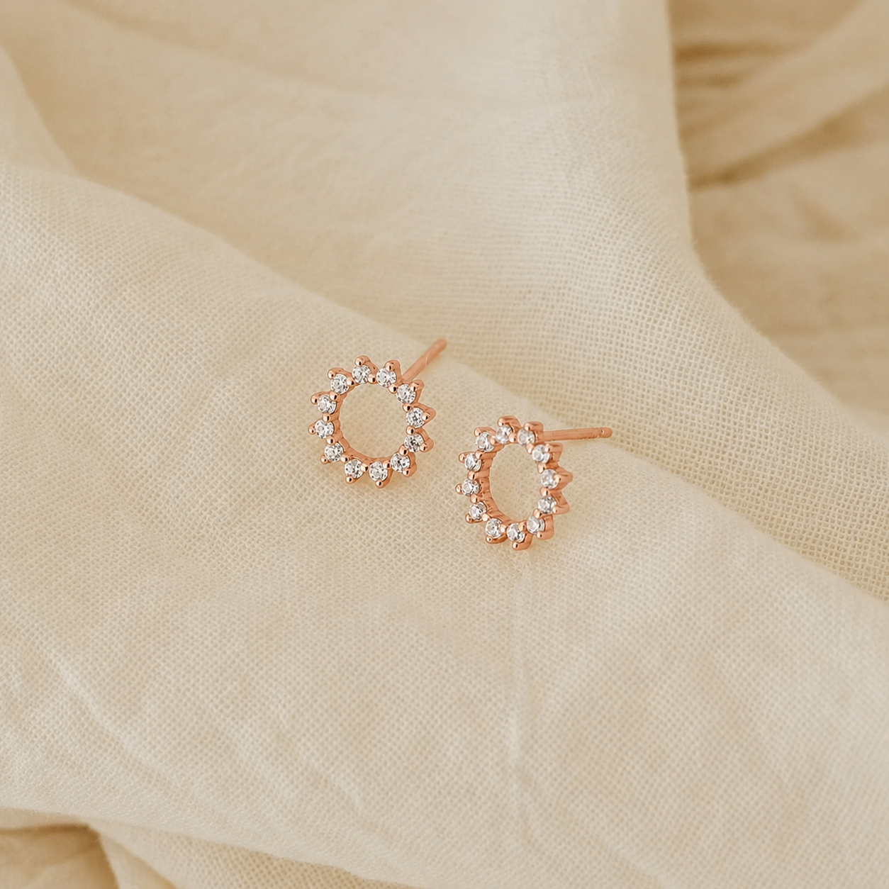 Rose gold hoop earrings with clear stones on a beige fabric background