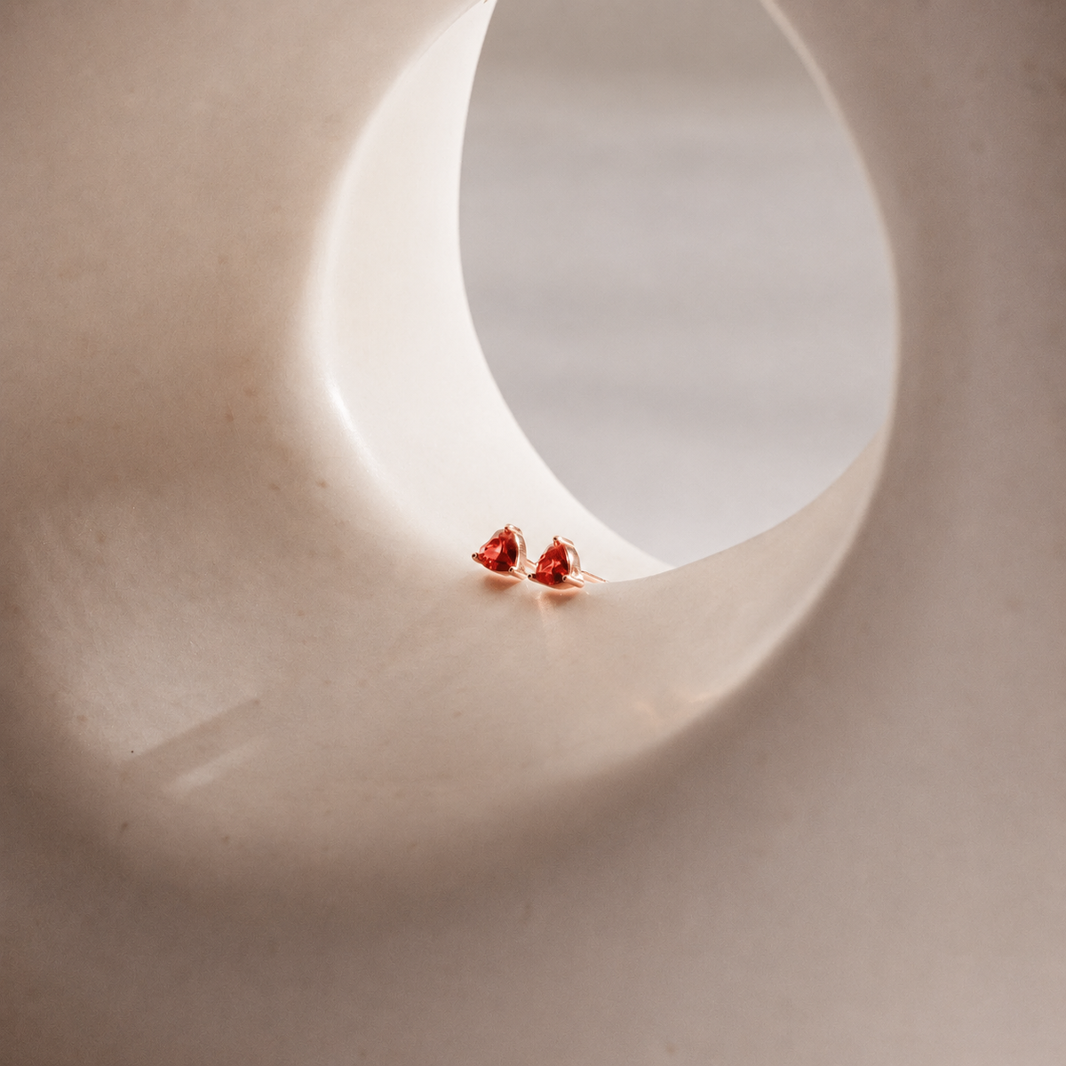 Small red earrings on a textured beige surface