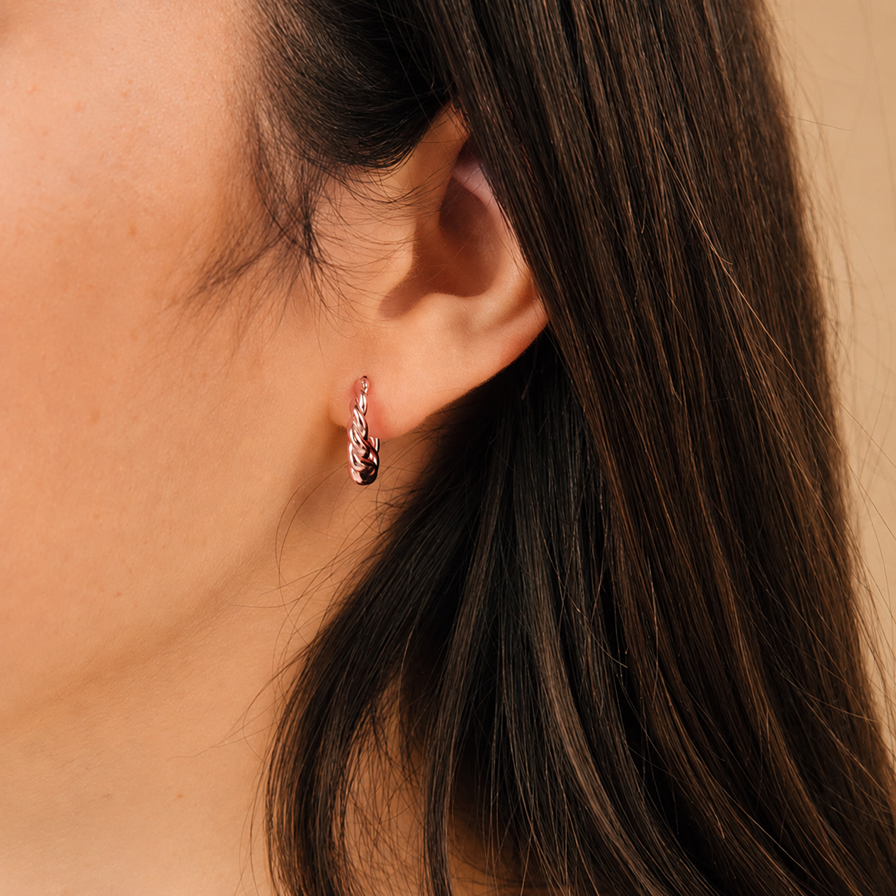 Close-up of an ear wearing a small hoop earring with dark hair and skin background